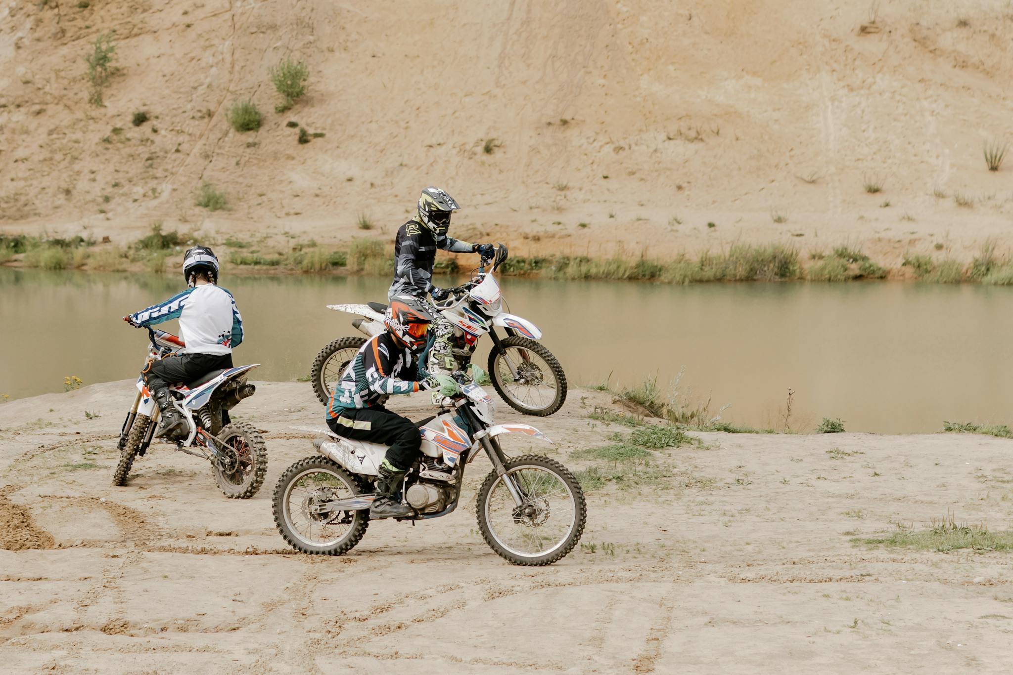 Three motocross riders enjoying an exciting off-road adventure near a serene lake.